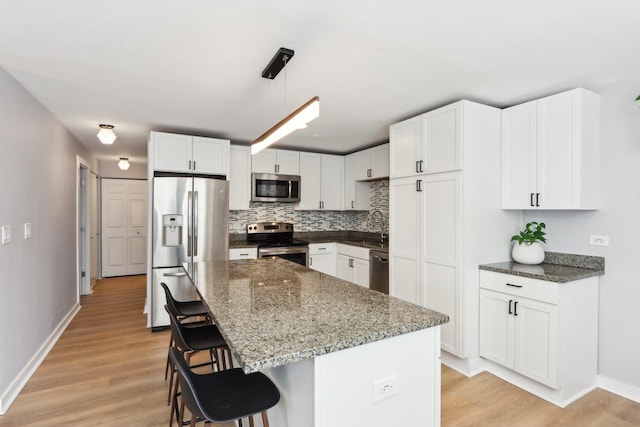 kitchen featuring light wood-style flooring, stainless steel appliances, white cabinetry, dark stone countertops, and a kitchen bar