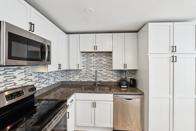 kitchen featuring decorative backsplash, appliances with stainless steel finishes, white cabinetry, a sink, and dark stone counters