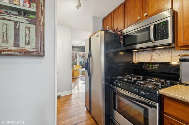 kitchen with stainless steel appliances, baseboards, backsplash, light wood finished floors, and brown cabinetry