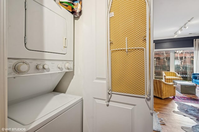 laundry area featuring laundry area, stacked washing maching and dryer, wood finished floors, and rail lighting