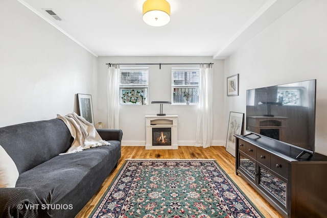 living room featuring baseboards, visible vents, wood finished floors, and a lit fireplace