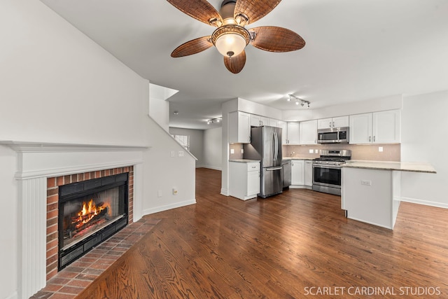 kitchen with stainless steel appliances, a peninsula, white cabinets, dark wood-style floors, and tasteful backsplash