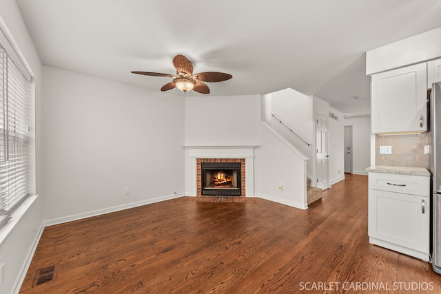 unfurnished living room with a brick fireplace, baseboards, visible vents, and dark wood-type flooring