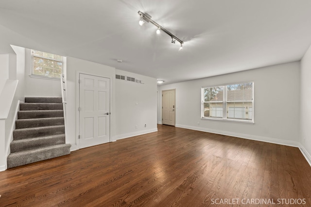 unfurnished living room featuring baseboards, visible vents, stairway, dark wood-style flooring, and track lighting