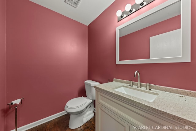 half bathroom with baseboards, visible vents, toilet, wood finished floors, and vanity