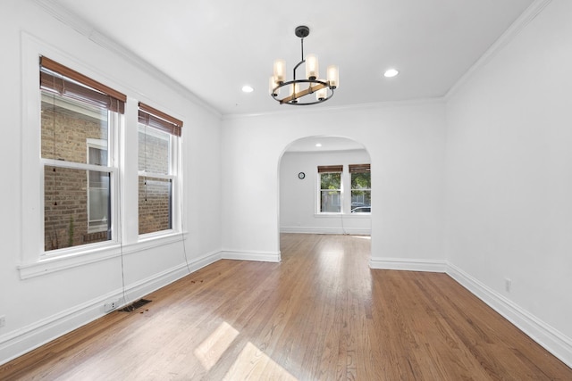 spare room featuring baseboards, arched walkways, wood finished floors, and ornamental molding