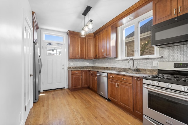 kitchen featuring dark countertops, appliances with stainless steel finishes, brown cabinets, light wood-type flooring, and a sink