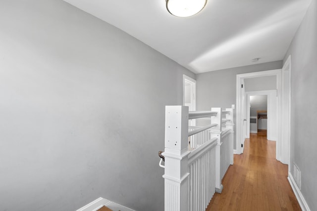 hallway with light wood-style floors, visible vents, an upstairs landing, and baseboards