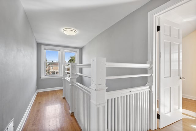 hall with an upstairs landing, wood finished floors, visible vents, and baseboards