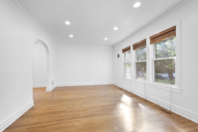 empty room featuring arched walkways, crown molding, and light wood-style flooring