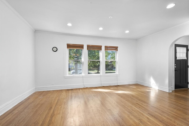 empty room with arched walkways, ornamental molding, wood finished floors, and baseboards