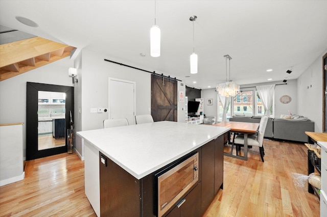 kitchen featuring open floor plan, a barn door, stainless steel microwave, and light wood-style flooring