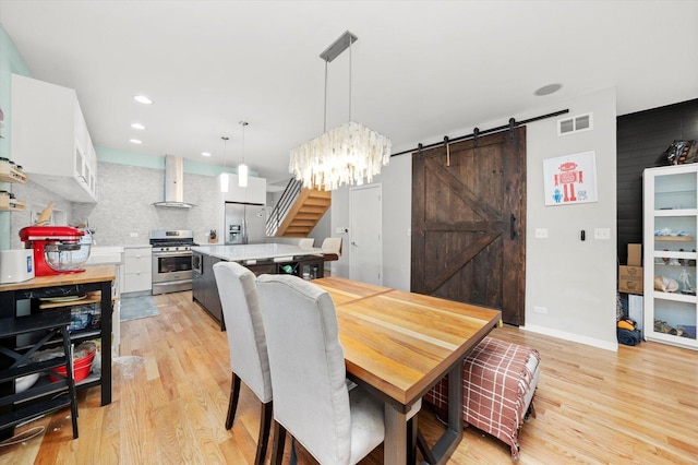 dining area featuring light wood-style floors, a barn door, stairway, and visible vents