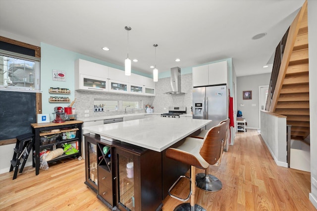 kitchen featuring a breakfast bar area, stainless steel appliances, white cabinets, light countertops, and wall chimney range hood