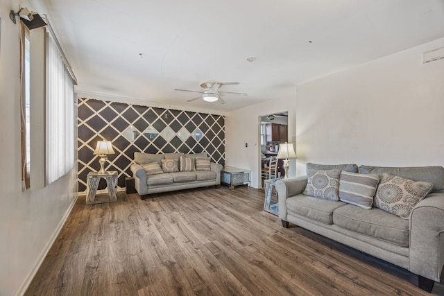 living area featuring ceiling fan, an accent wall, baseboards, and wood finished floors