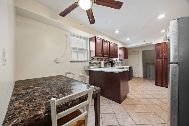 kitchen with light tile patterned floors, tasteful backsplash, freestanding refrigerator, a sink, and a peninsula