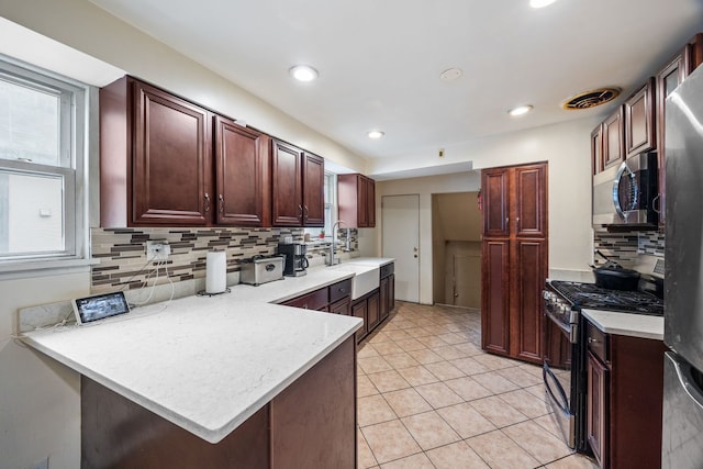 kitchen with appliances with stainless steel finishes, a peninsula, light countertops, a sink, and light tile patterned flooring