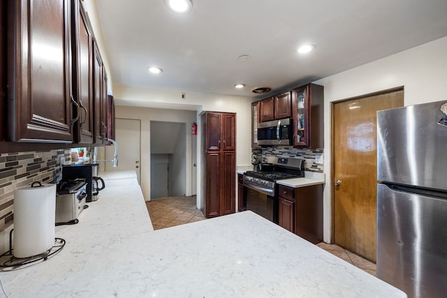 kitchen featuring light tile patterned floors, appliances with stainless steel finishes, backsplash, and glass insert cabinets