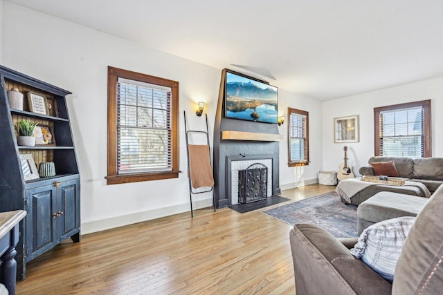 living area featuring light wood-style flooring, baseboards, and a fireplace with flush hearth