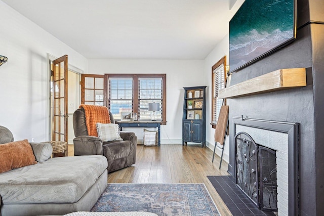 living room featuring a fireplace with flush hearth, hardwood / wood-style flooring, and baseboards