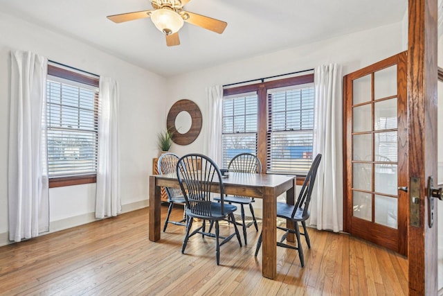 dining space featuring light wood-style floors, a ceiling fan, baseboards, and a wealth of natural light