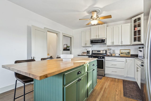 kitchen featuring white cabinets, butcher block countertops, appliances with stainless steel finishes, a kitchen breakfast bar, and green cabinets