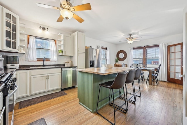 kitchen with butcher block counters, a kitchen breakfast bar, stainless steel appliances, open shelves, and a sink