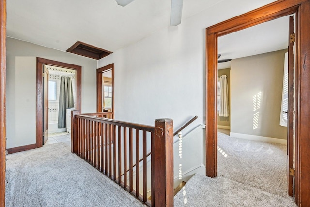 corridor featuring carpet floors, baseboards, and an upstairs landing