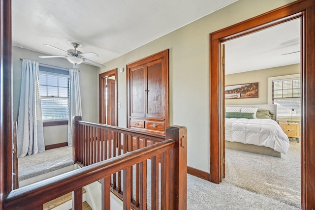 hallway featuring a healthy amount of sunlight, baseboards, light colored carpet, and an upstairs landing