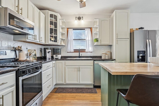 kitchen featuring a sink, light wood-style floors, appliances with stainless steel finishes, backsplash, and open shelves