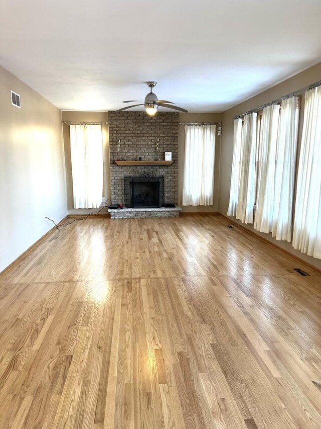 unfurnished living room featuring light wood-type flooring, a fireplace, visible vents, and a ceiling fan