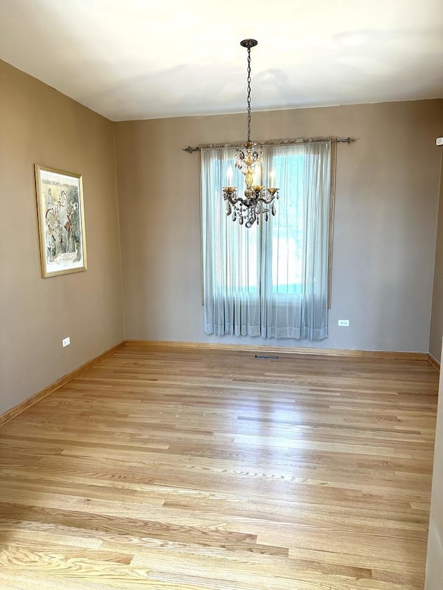 empty room featuring light wood-style floors, baseboards, and an inviting chandelier