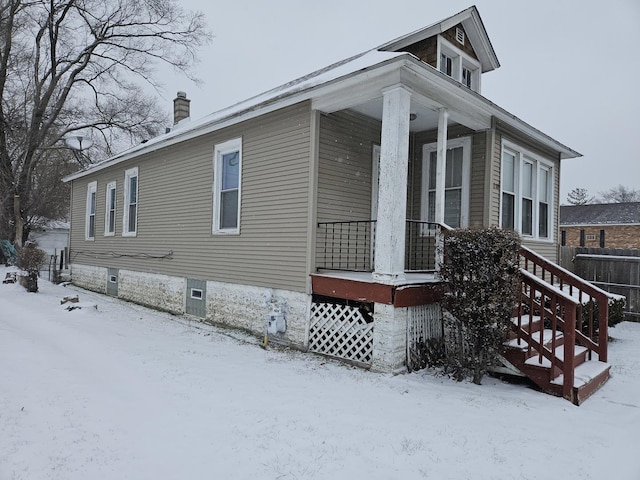 snow covered property featuring covered porch and a chimney