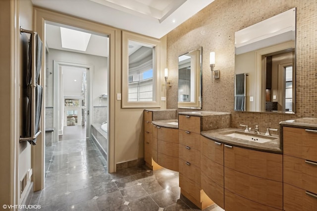 full bath featuring a skylight, two vanities, a sink, and backsplash