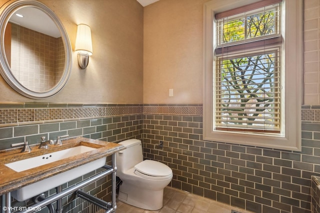 half bath with tile walls, toilet, wainscoting, a sink, and tile patterned floors