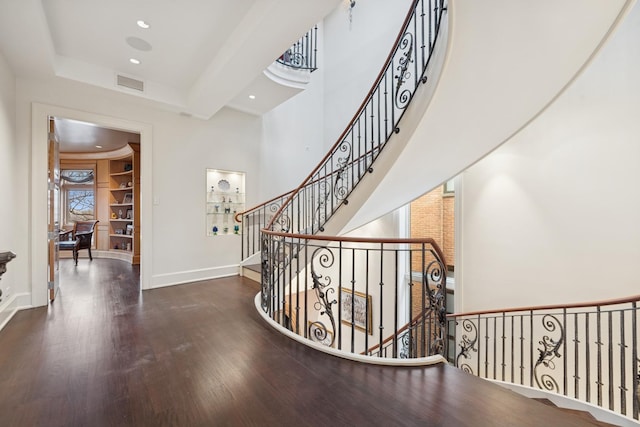 stairway featuring baseboards, visible vents, a towering ceiling, wood finished floors, and recessed lighting