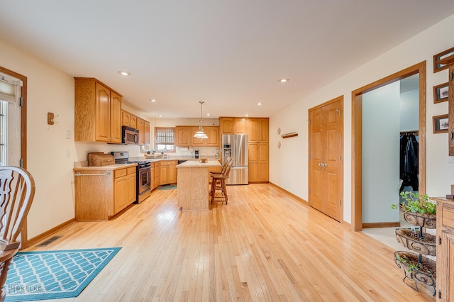 kitchen featuring light wood-style flooring, appliances with stainless steel finishes, a breakfast bar area, a center island, and light countertops