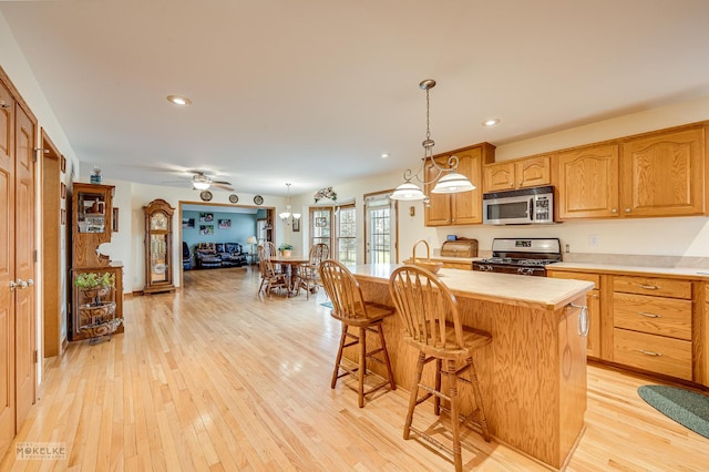 kitchen featuring decorative light fixtures, stainless steel appliances, light countertops, light wood-type flooring, and a kitchen breakfast bar