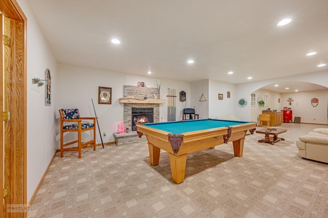 rec room with arched walkways, a stone fireplace, recessed lighting, and light colored carpet