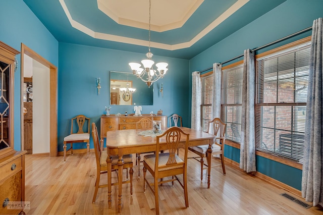 dining room with a tray ceiling, a notable chandelier, visible vents, light wood-style floors, and baseboards