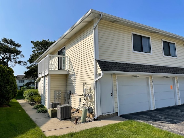 view of side of property featuring a shingled roof, an attached garage, central AC unit, a balcony, and driveway