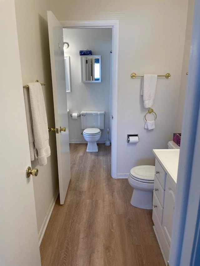 bathroom featuring toilet, baseboards, wood finished floors, and vanity