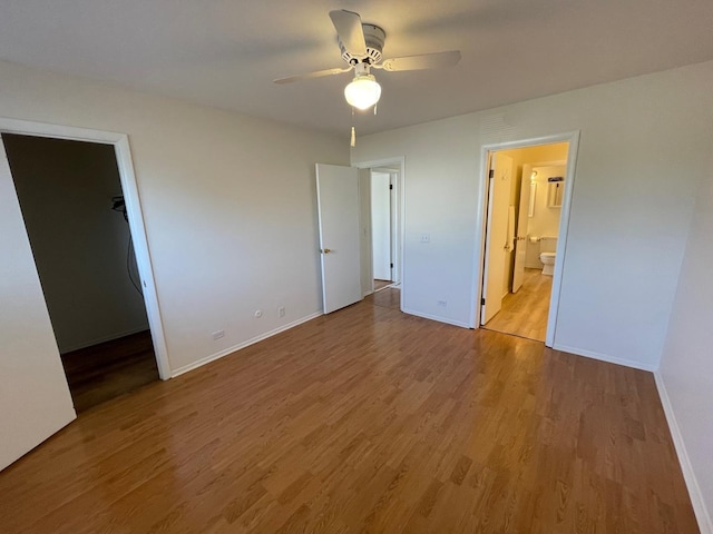 unfurnished bedroom with a spacious closet, baseboards, and wood finished floors