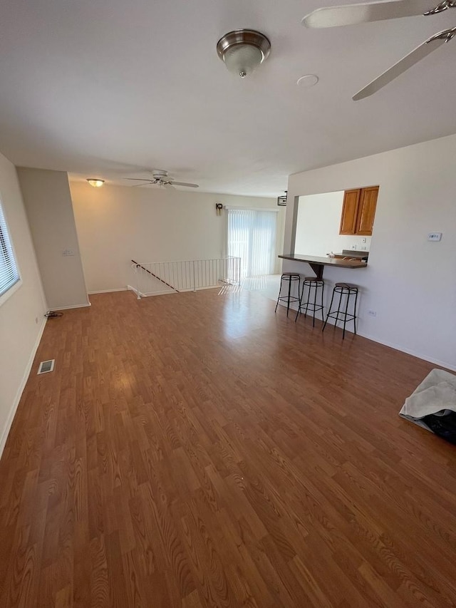 unfurnished living room featuring visible vents, wood finished floors, a ceiling fan, and baseboards