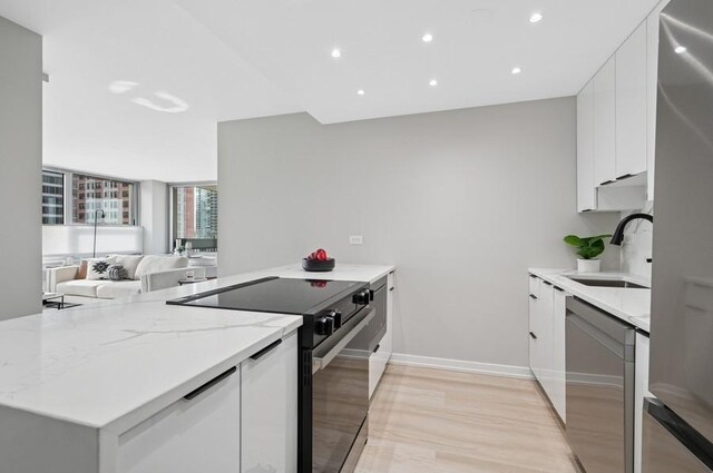 kitchen featuring light stone counters, stainless steel appliances, white cabinetry, a sink, and modern cabinets