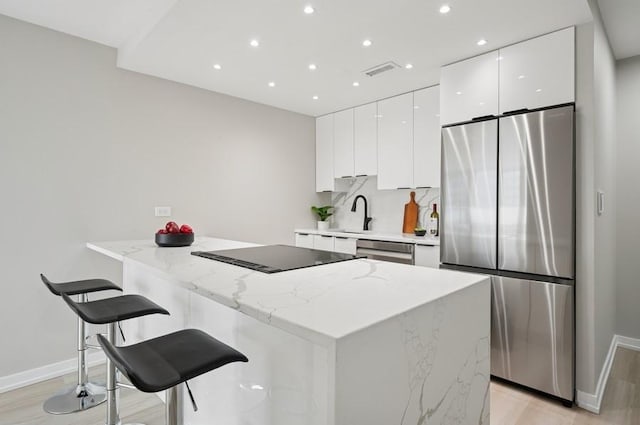 kitchen with visible vents, white cabinets, modern cabinets, a kitchen breakfast bar, and stainless steel appliances