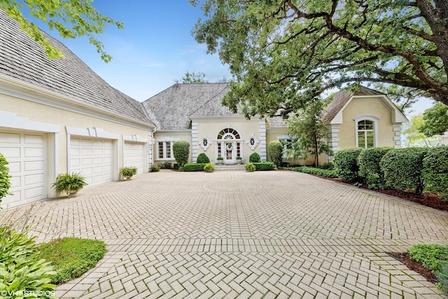 view of front facade featuring a garage, french doors, decorative driveway, stucco siding, and a high end roof