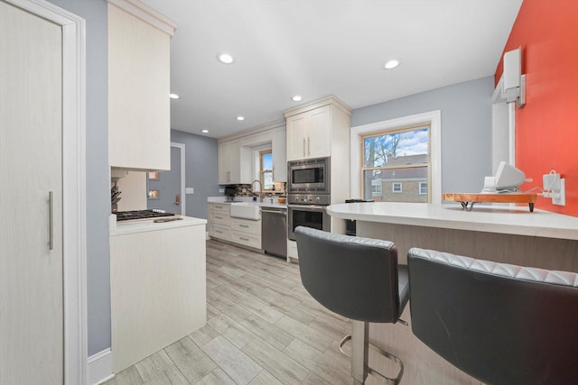 kitchen with appliances with stainless steel finishes, a sink, light countertops, light wood-style floors, and backsplash