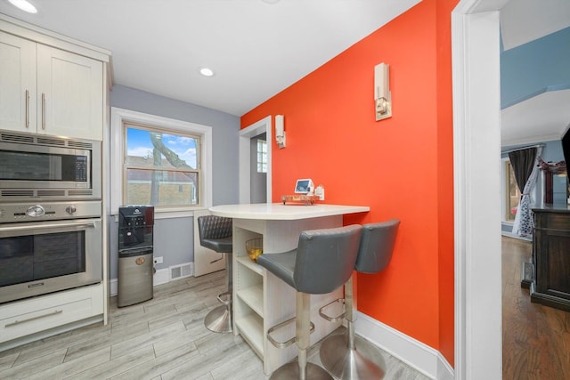 kitchen featuring stainless steel appliances, visible vents, baseboards, light wood-style floors, and a kitchen bar