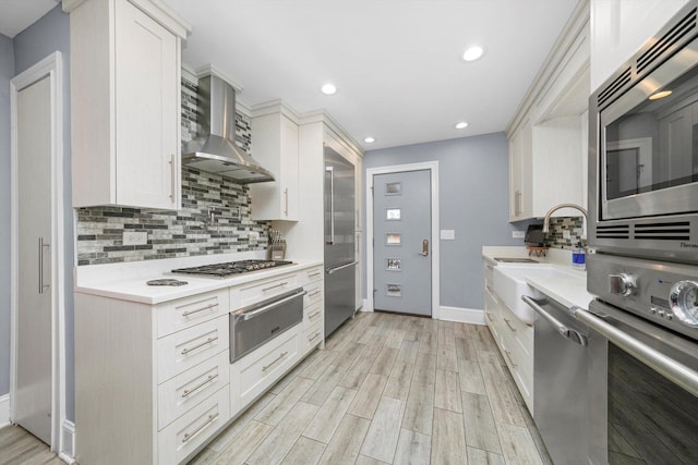 kitchen with light countertops, appliances with stainless steel finishes, backsplash, a warming drawer, and wall chimney exhaust hood